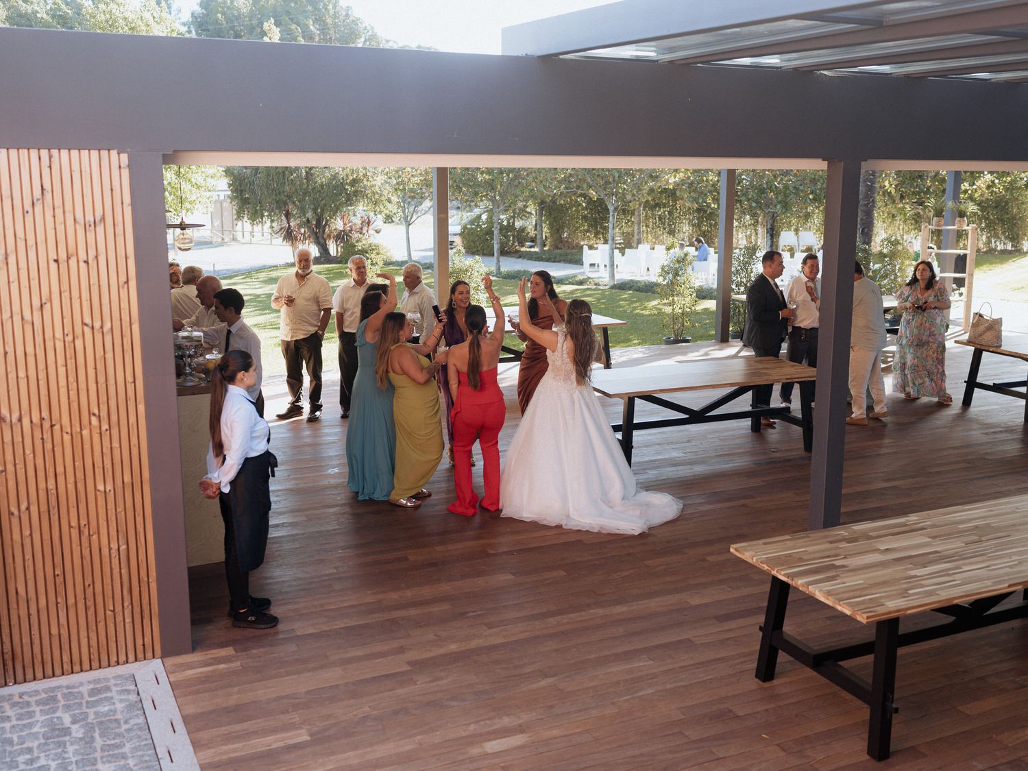 A covered outdoor patio area set up for a gathering with tables and chairs under a slatted wooden roof.