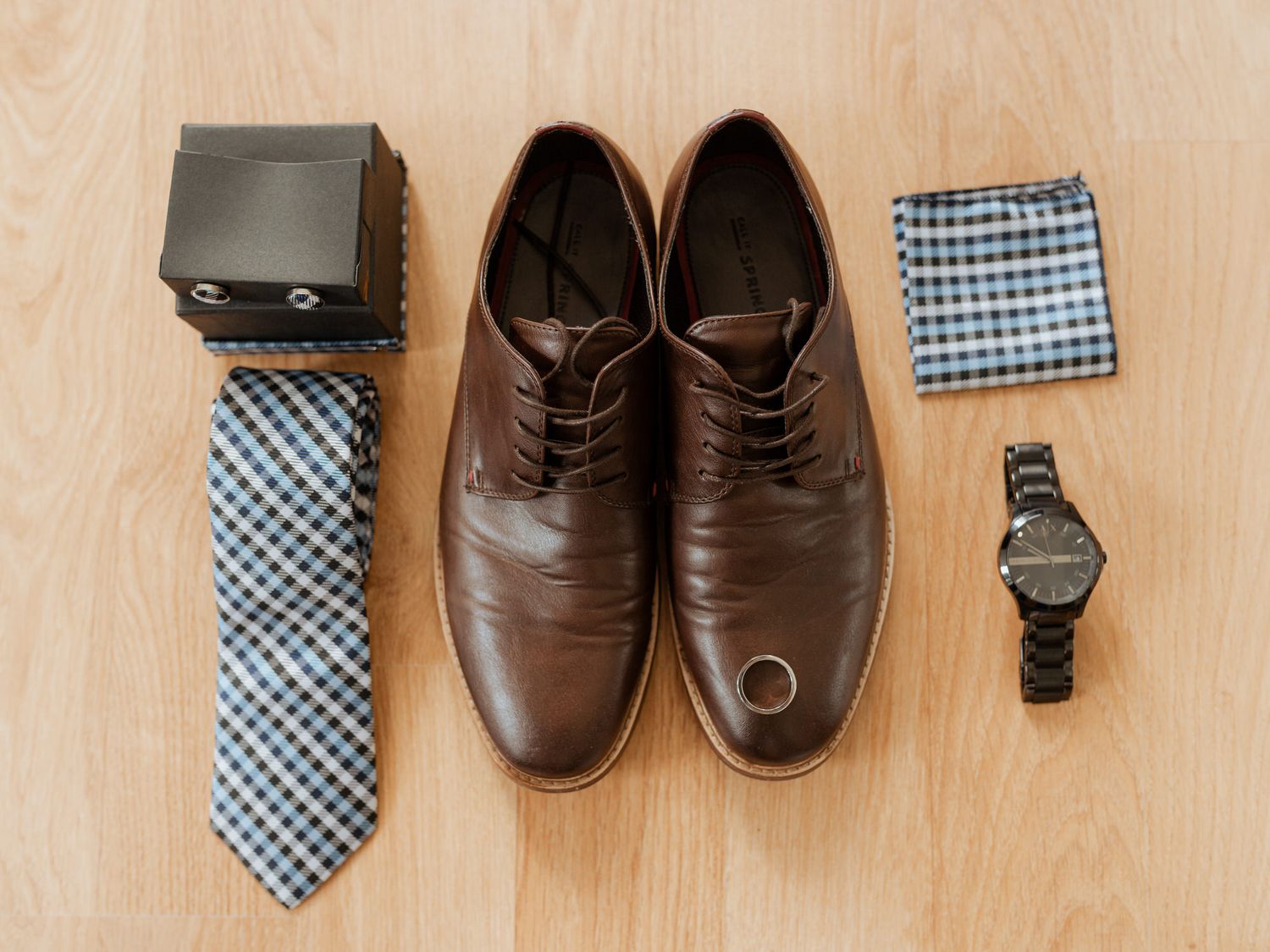 Dark brown leather dress shoes arranged with blue gingham neckties and accessories against a neutral background.