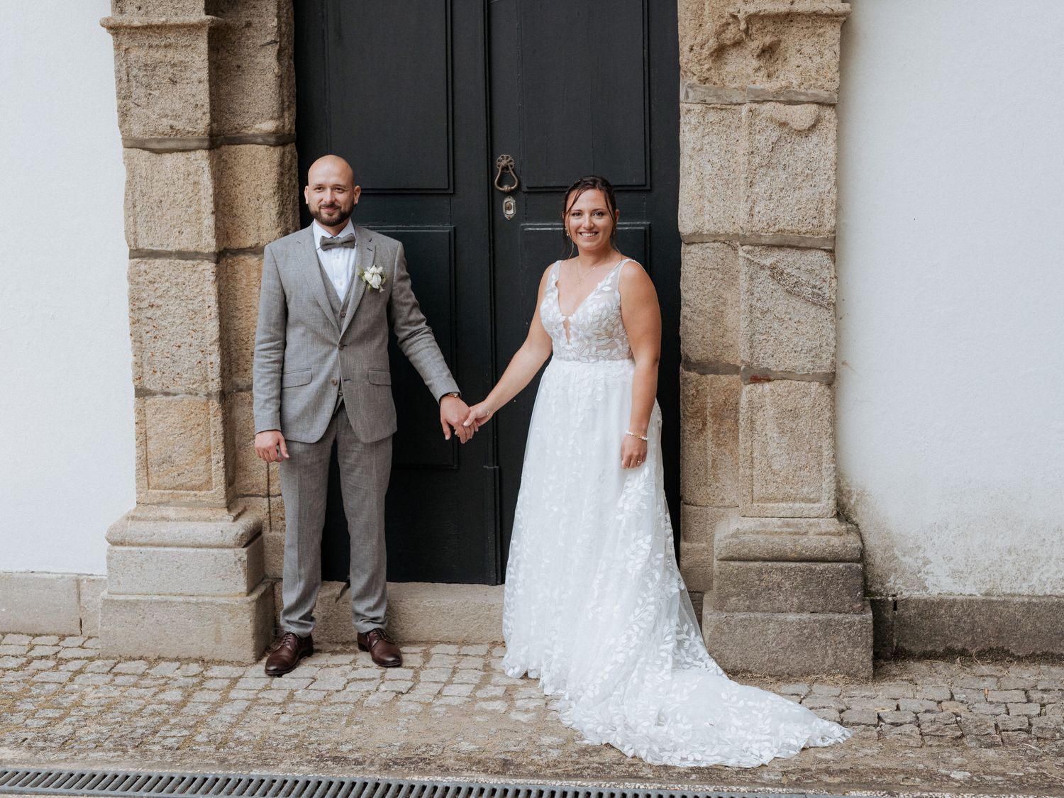 A newlywed couple poses in front of an elegant black door framed by stone pillars at their wedding.