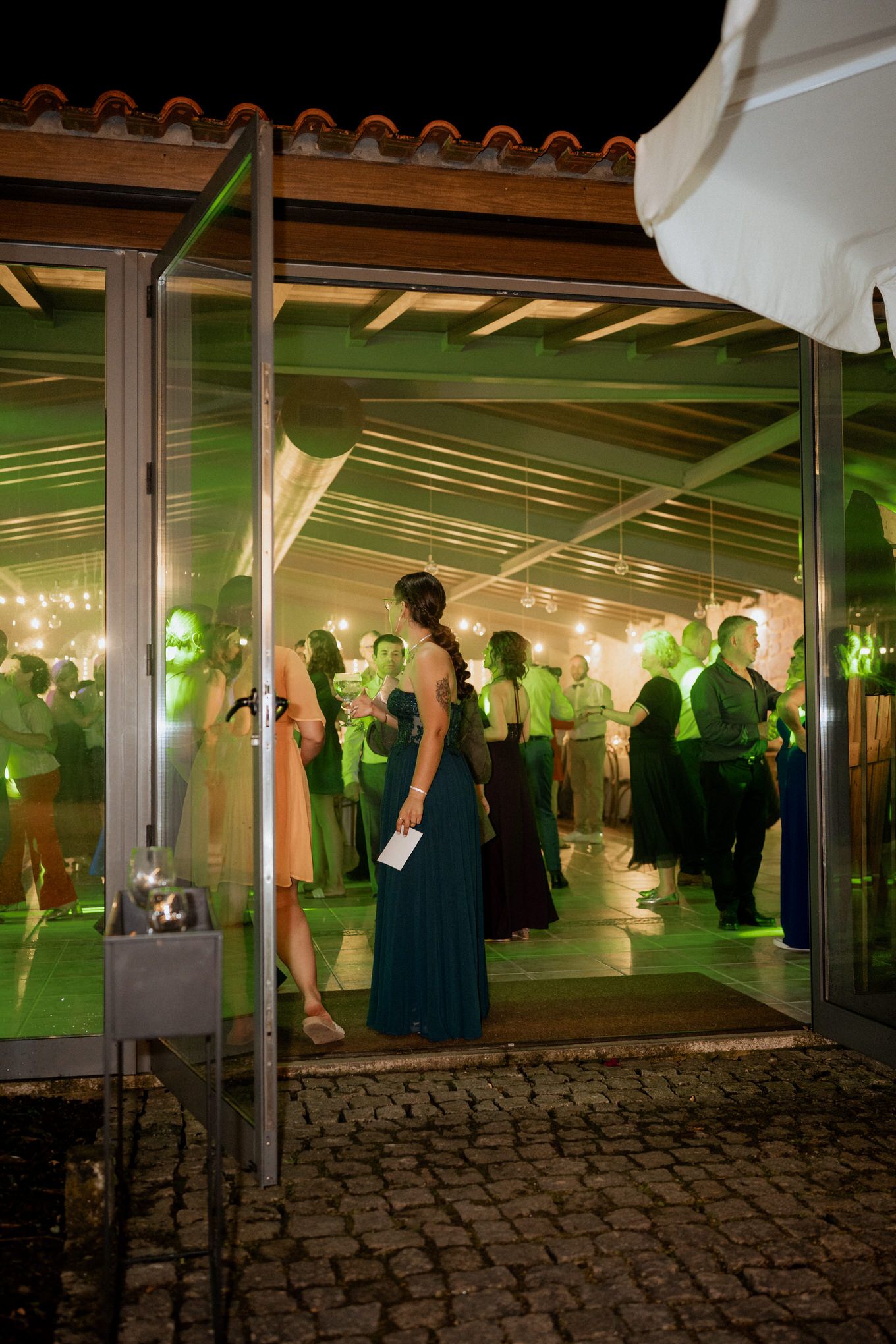Evening event under a covered patio with green lighting and guests in formal attire mingling at an outdoor venue.