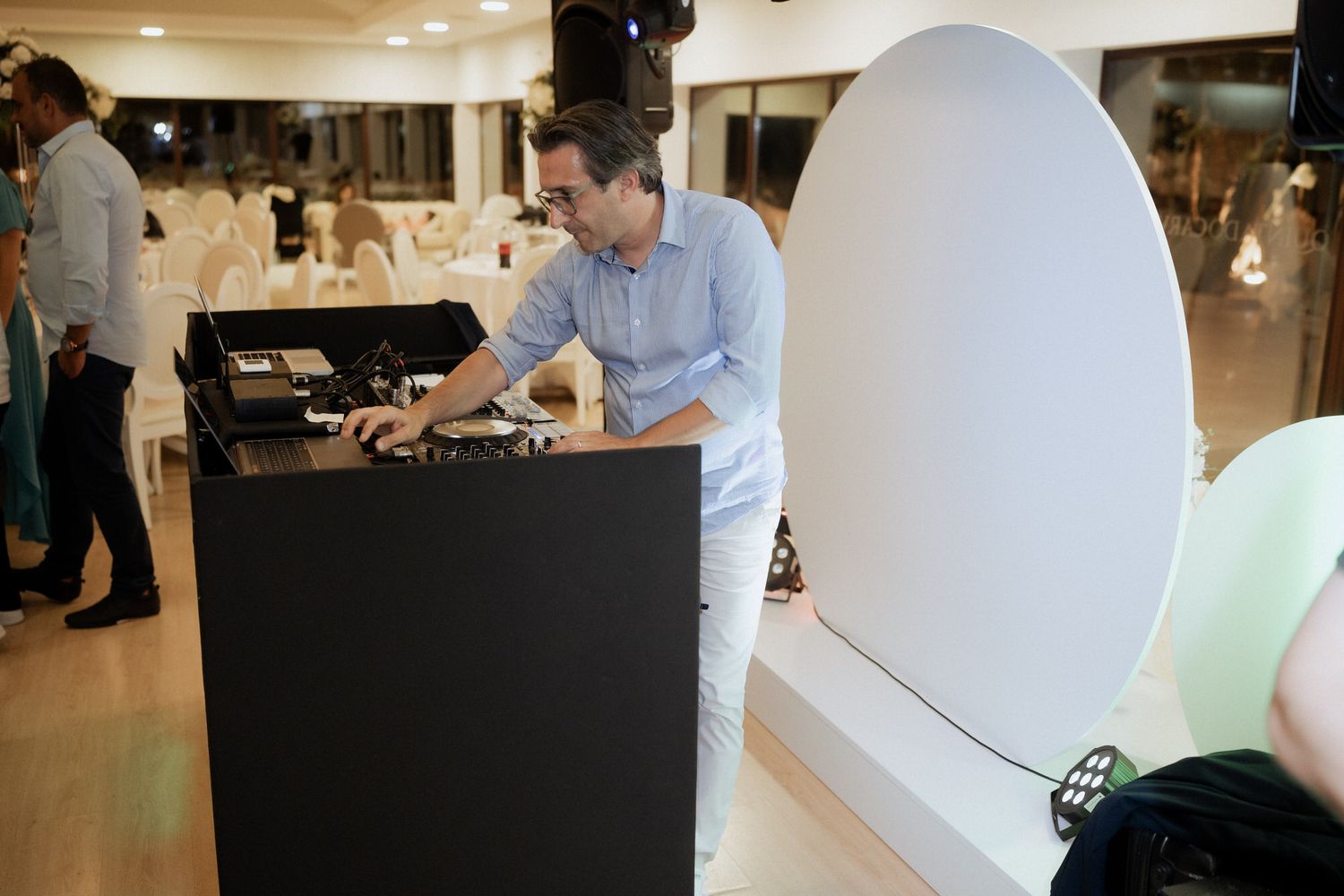 DJ mixing music at an event with mixing equipment on a black stand in a modern indoor space with white walls.