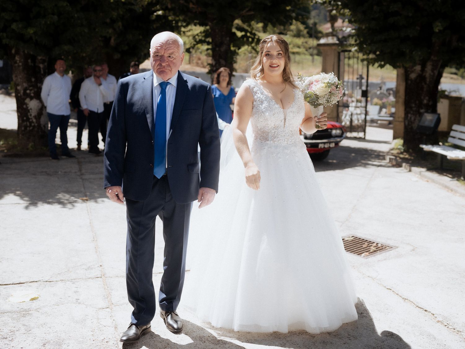 A pair walking together outdoors, with one wearing a navy suit and the other in an elegant white wedding gown.