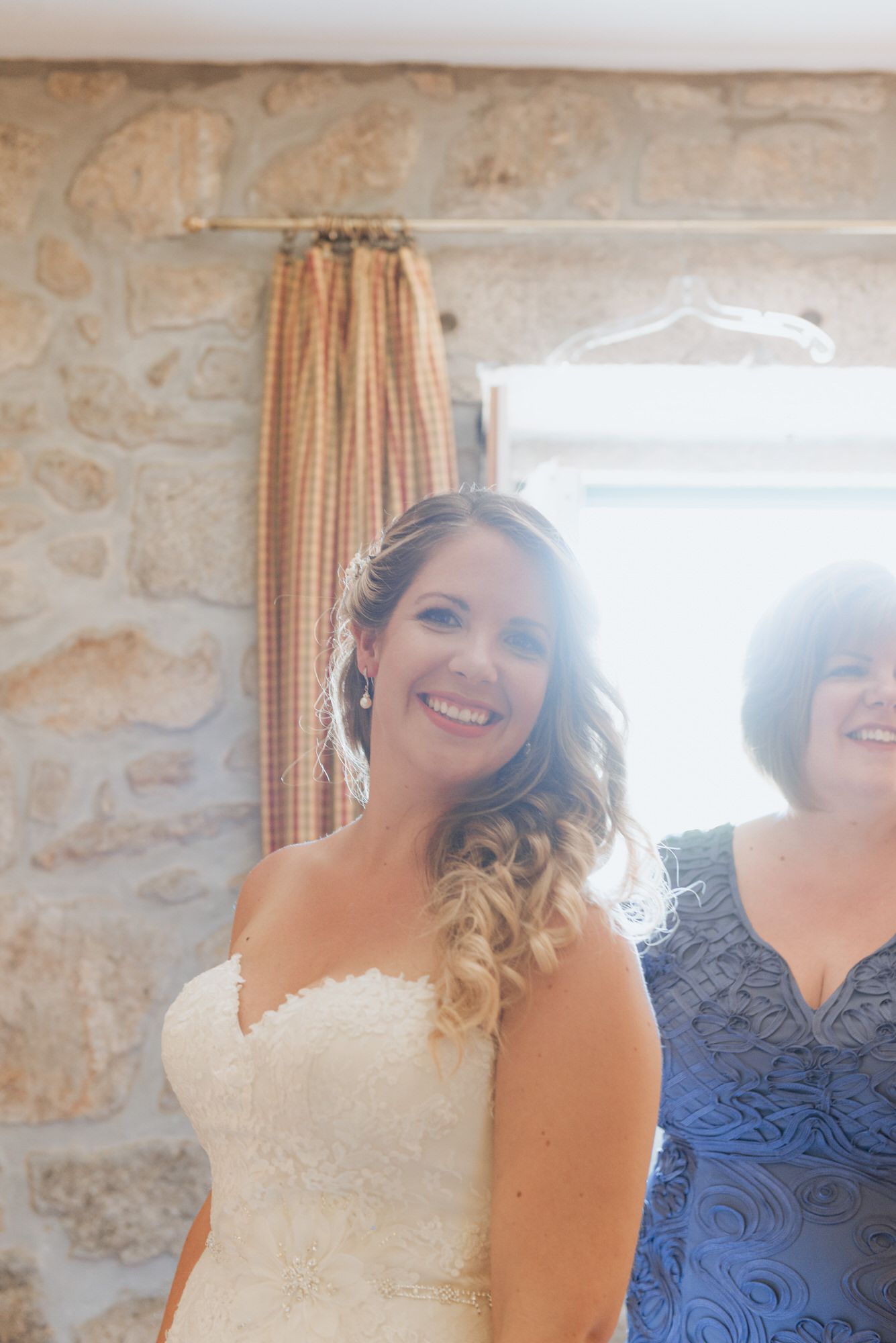 A bride in a white lace sweetheart neckline wedding dress stands near a stone wall with natural lighting.