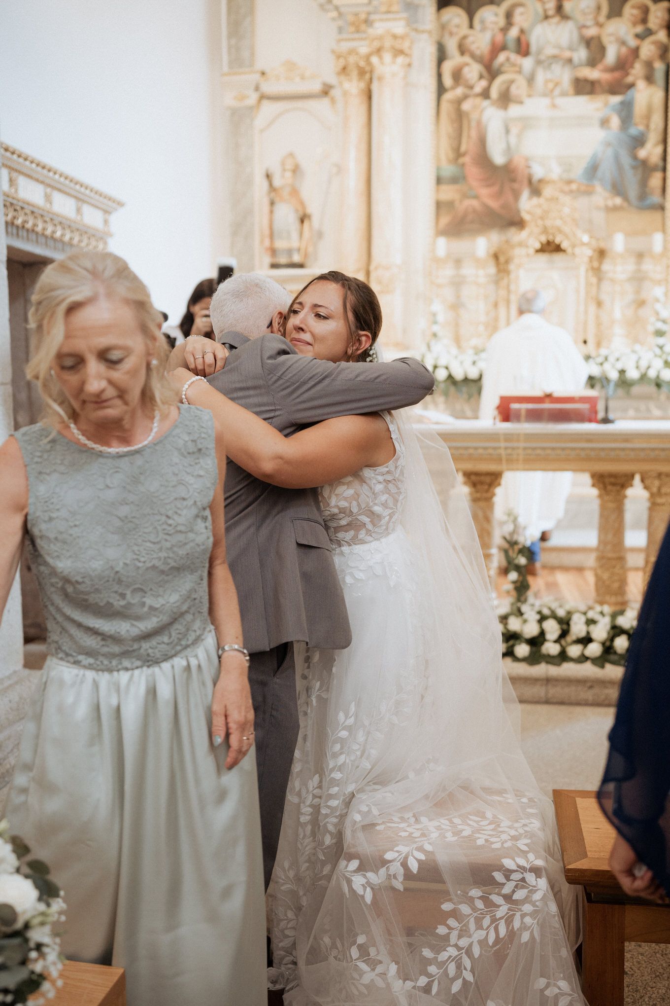 Touching moment of people embracing during a wedding ceremony inside an ornate church with floral decorations.