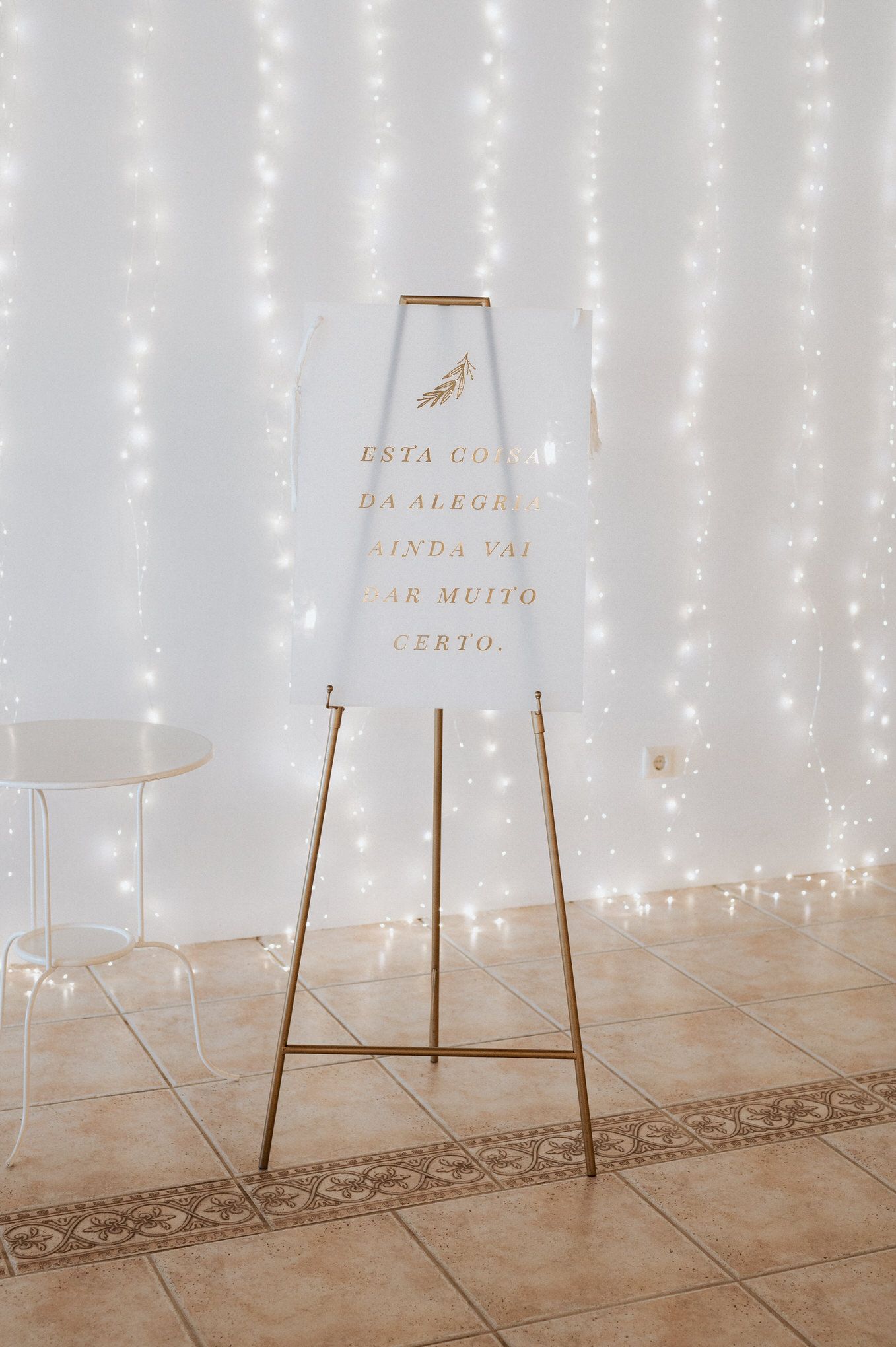 Illuminated white wedding sign on gold stand with twinkle light backdrop and tiled floor.