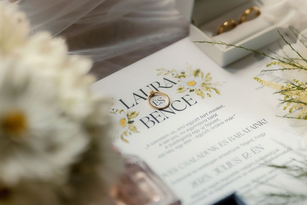 Elegant wedding invitation with gold lettering and white flowers in soft focus.