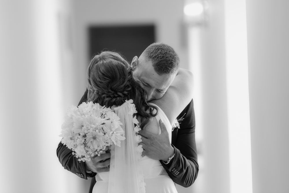 A romantic black and white wedding photo shows a couple sharing an intimate kiss in a soft, elegant setting.