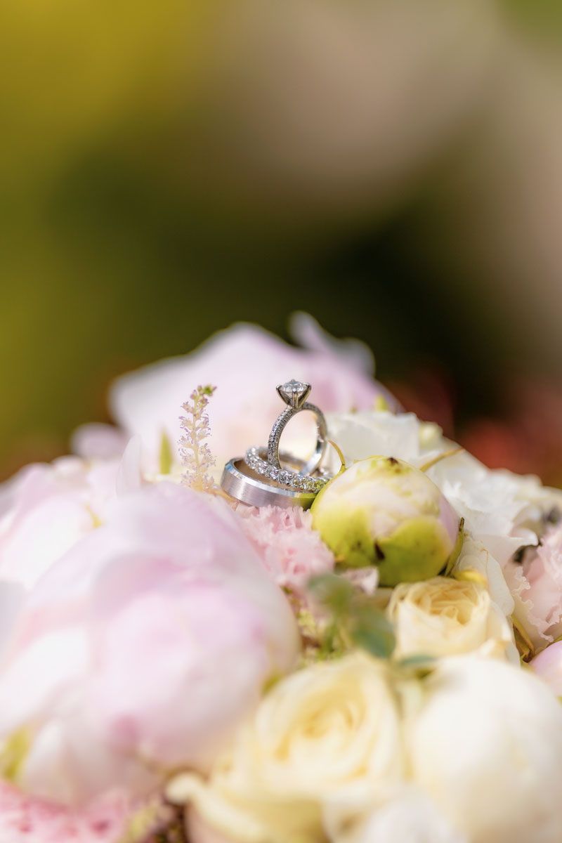 Elegant engagement ring nestled among soft pink and white flower petals in a romantic wedding setting.