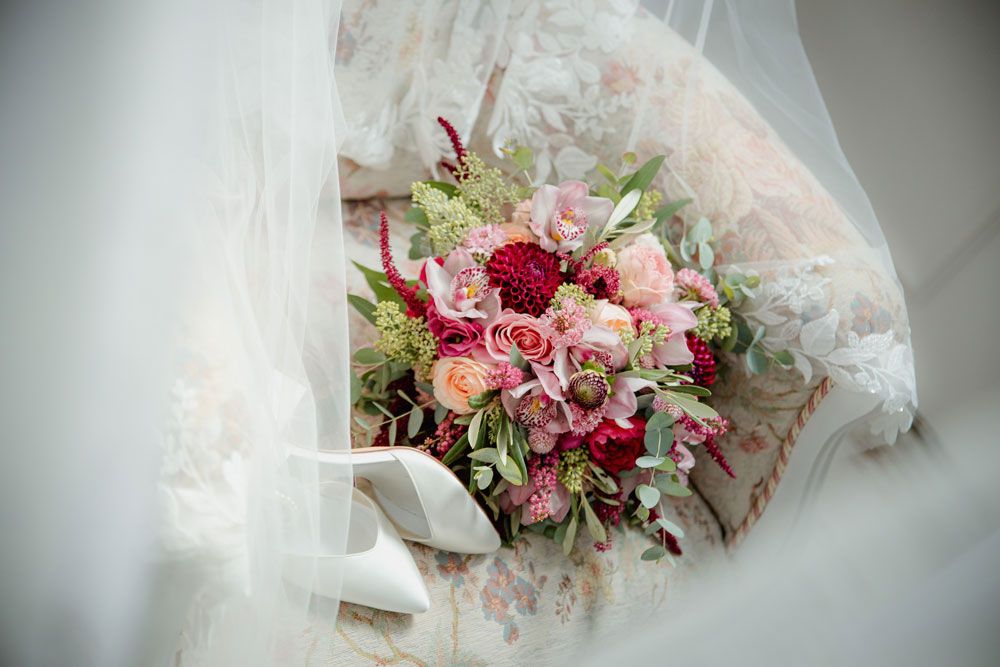 A delicate pink and white floral bouquet with roses and orchids wrapped in sheer fabric creates an elegant bridal arrangement.