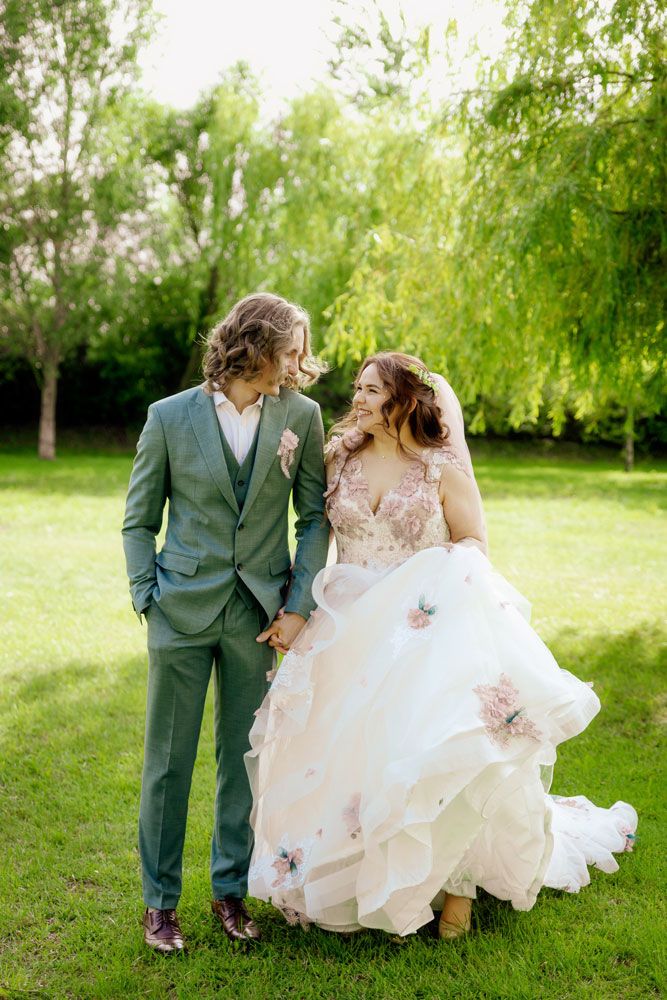 Wedding couple walking together through a lush green garden with flowing white dress and grey suit.