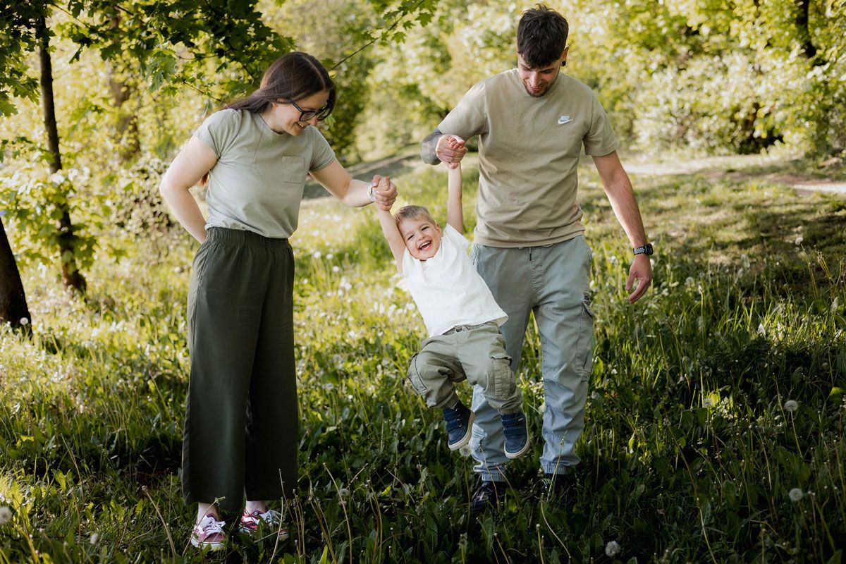 Family of three in matching green outfits swinging child between them in a sunny park.