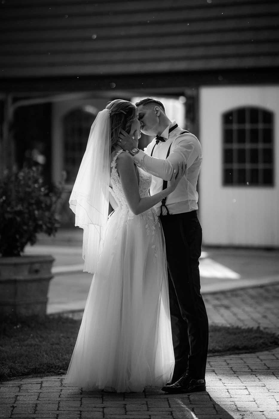 A romantic black and white wedding photo showing a tender moment between newlyweds on a brick patio.