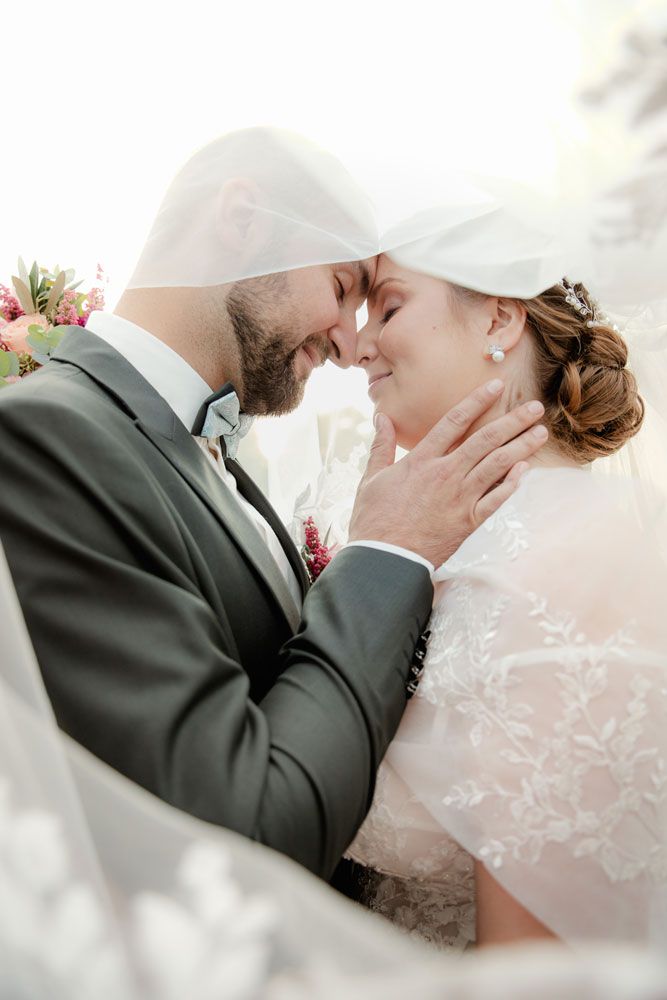 Romantic wedding portrait of couple in intimate embrace with bride in lace dress and groom in gray suit.