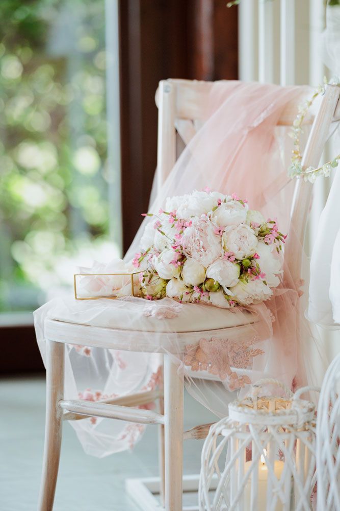 Elegant white chairs adorned with soft pink tulle and delicate floral arrangements create a romantic wedding setting.