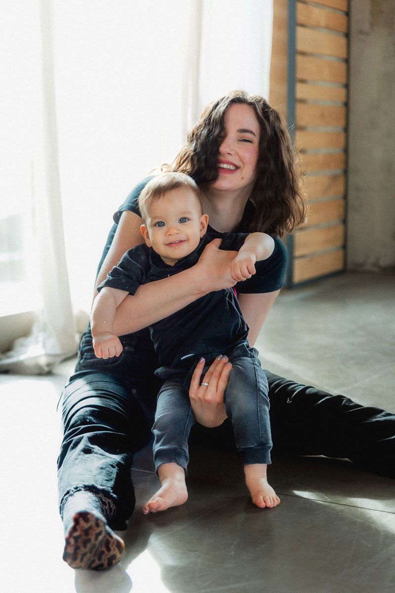 A happy young mother sitting on the floor, smiling while holding her cute baby in a bright room.