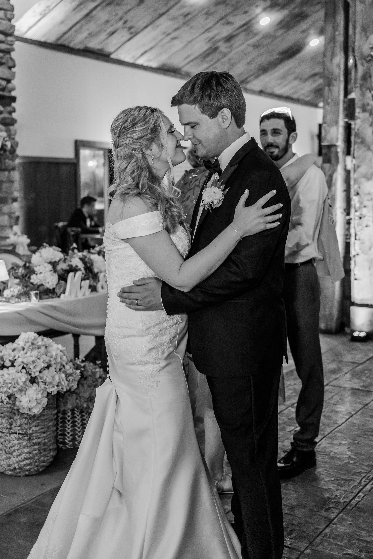 Black and white photos showing a couple dancing together at a rustic indoor wedding venue.