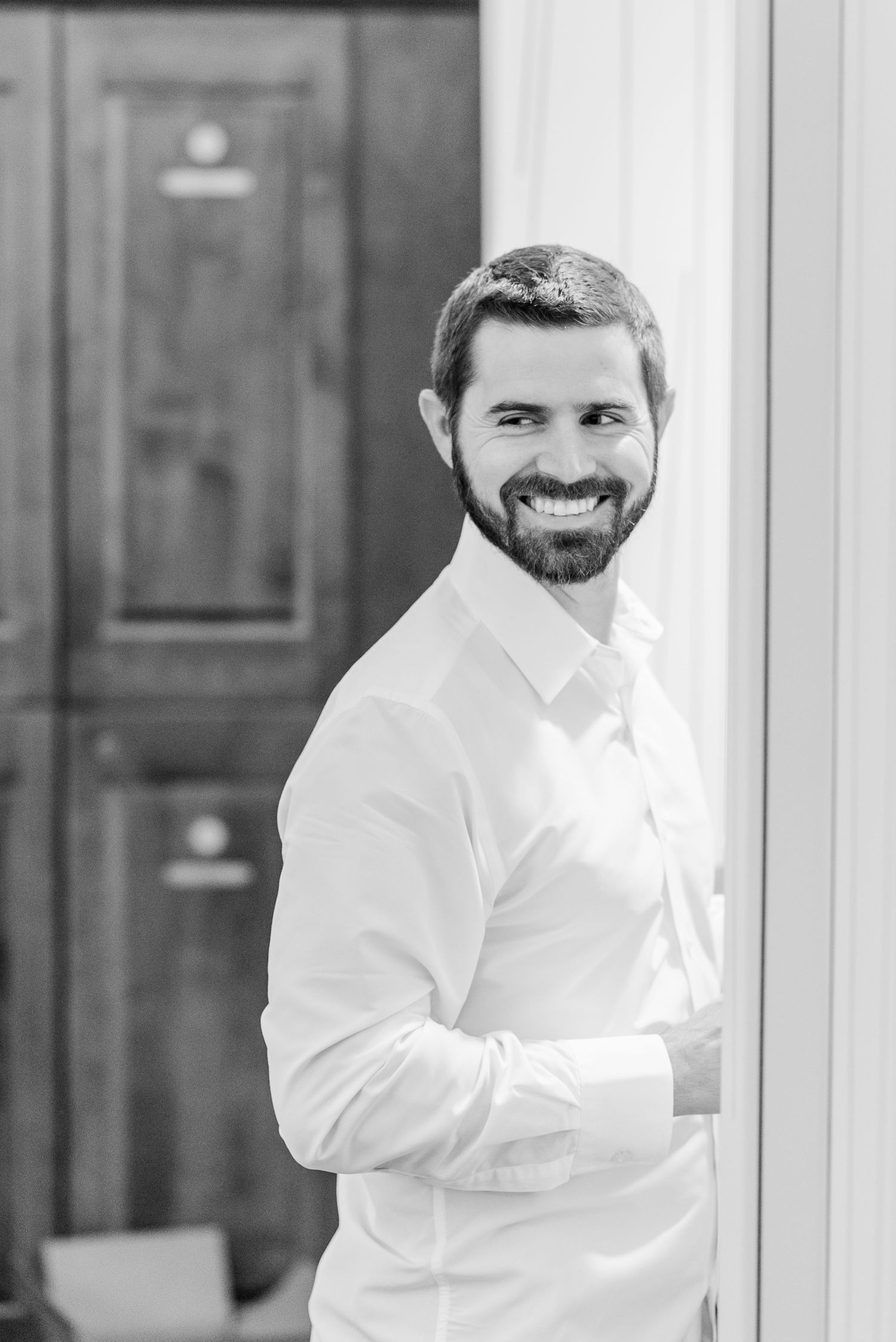 A person in a white button-down shirt smiles while looking off to the side in a professional indoor setting.