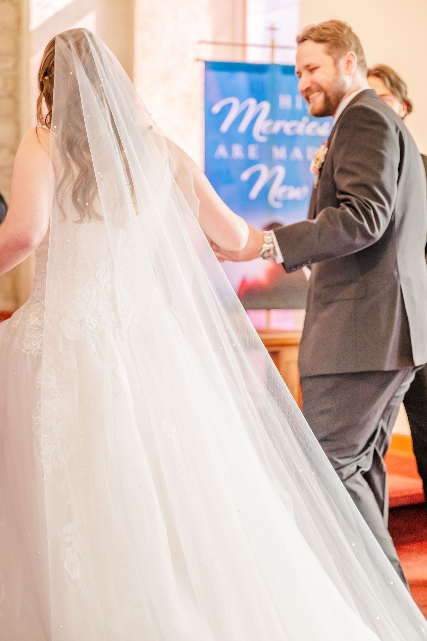 Wedding ceremony scene with flowing white veil and dress train in a church setting.