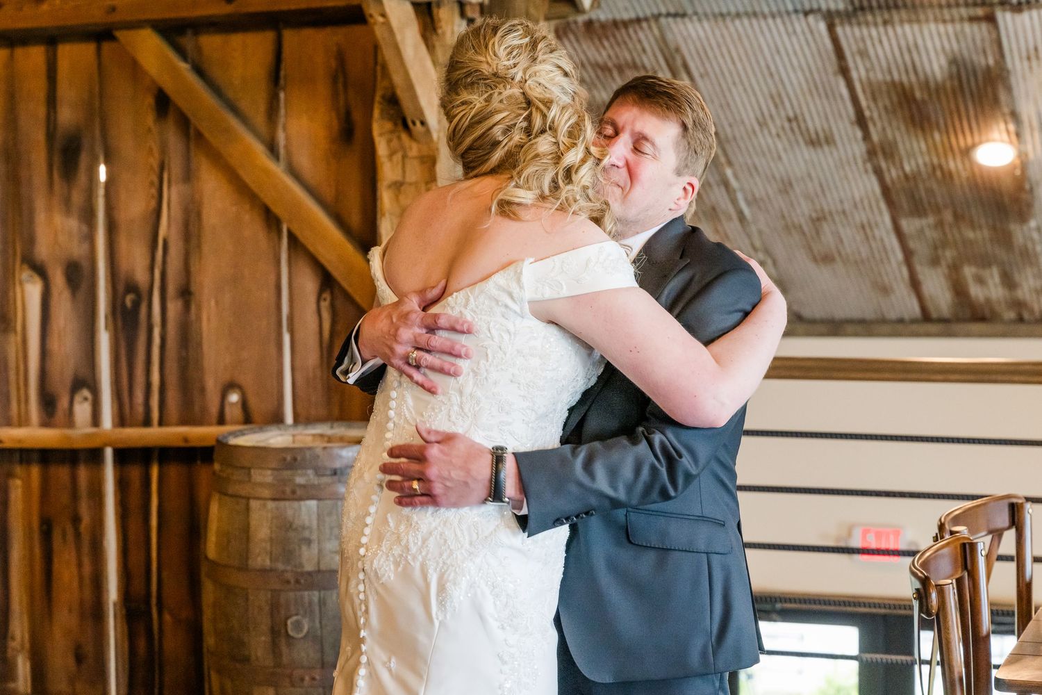 A couple embraces during their first look moment inside a rustic barn venue. The Old Barns at Dry Run Farms in Williamsport, OH.