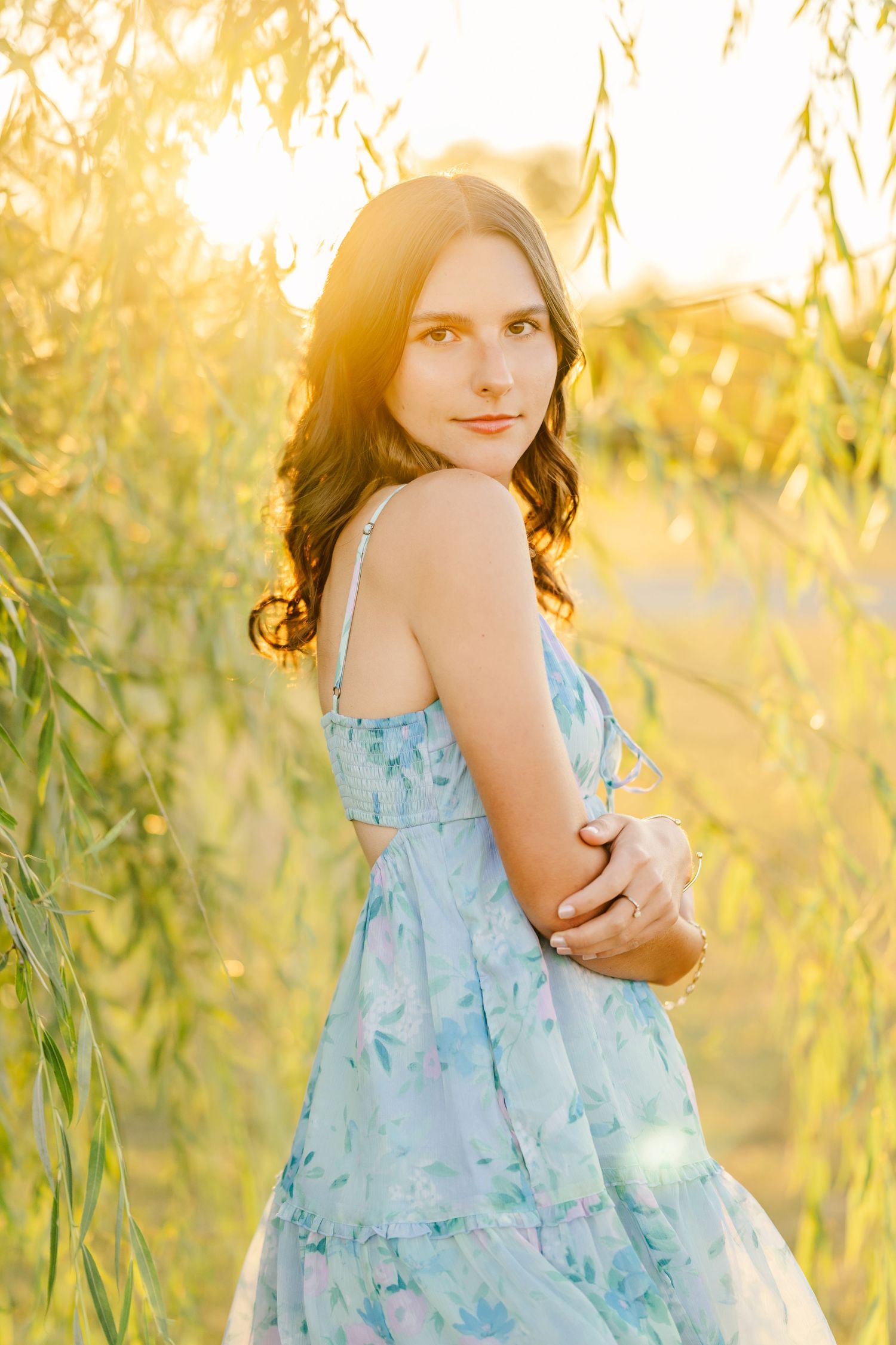 A light blue sundress flows gracefully in a golden sunlit field of tall grass and willow branches.