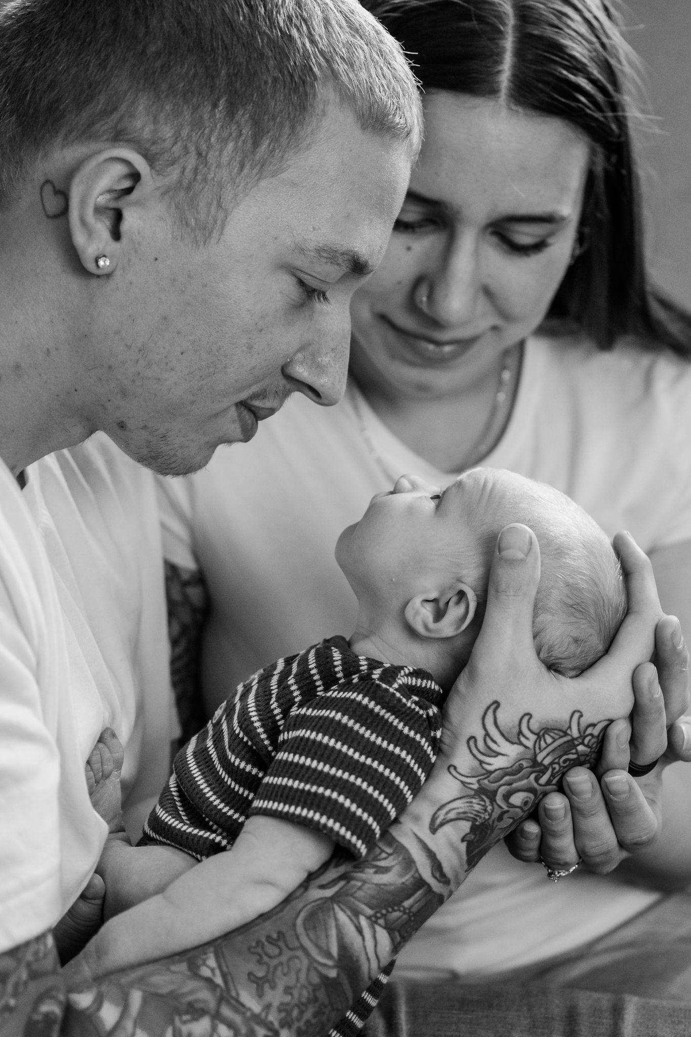 Black and white photo of tattooed parents lovingly cradling their newborn baby together.