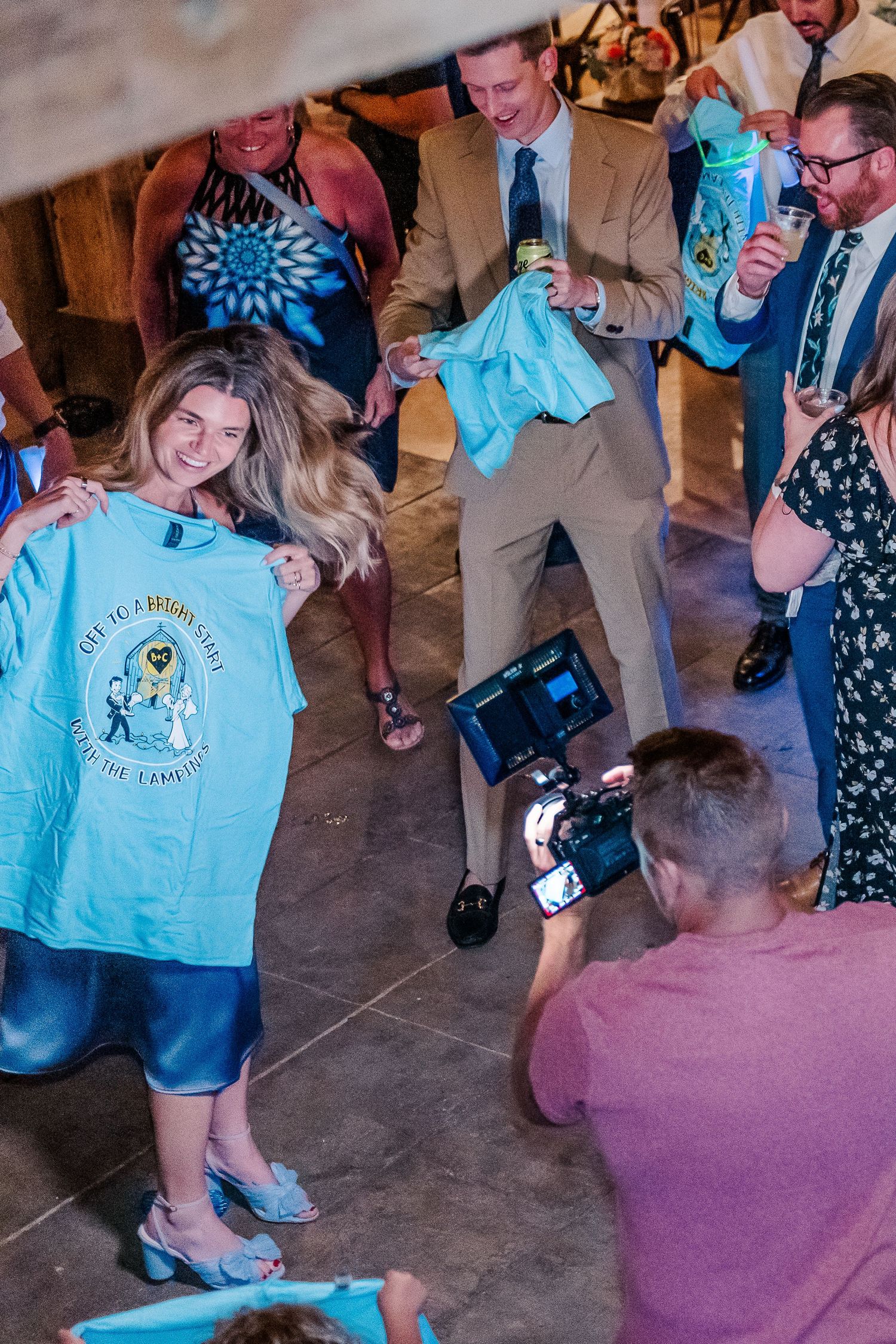 Wedding guests displaying custom t-shirts while being photographed at a reception venue.