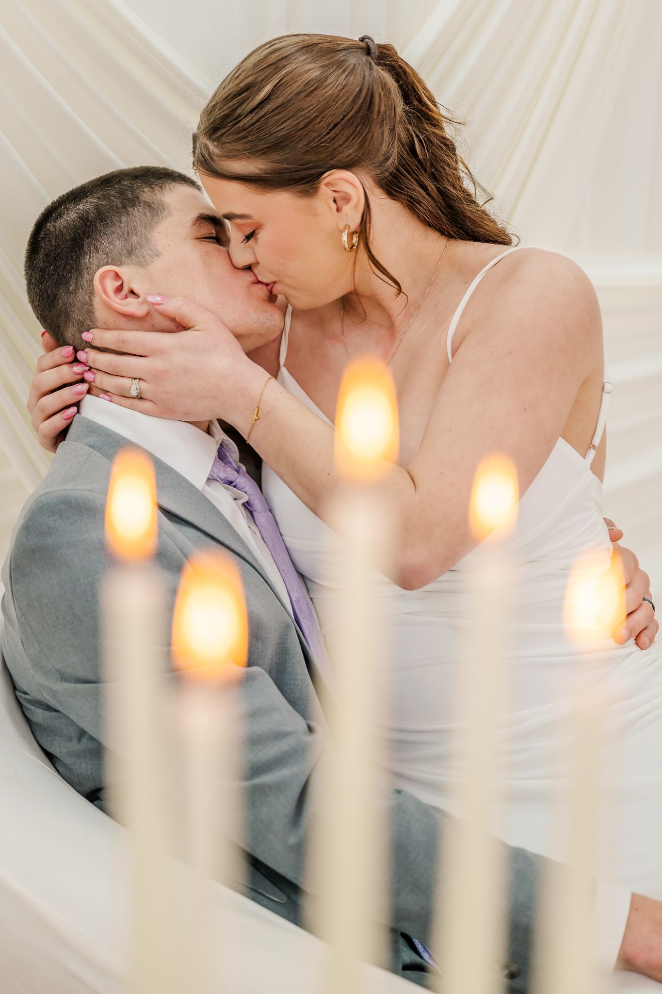 Bride and groom share a romantic kiss surrounded by glowing candlelight at their elegant wedding ceremony.
