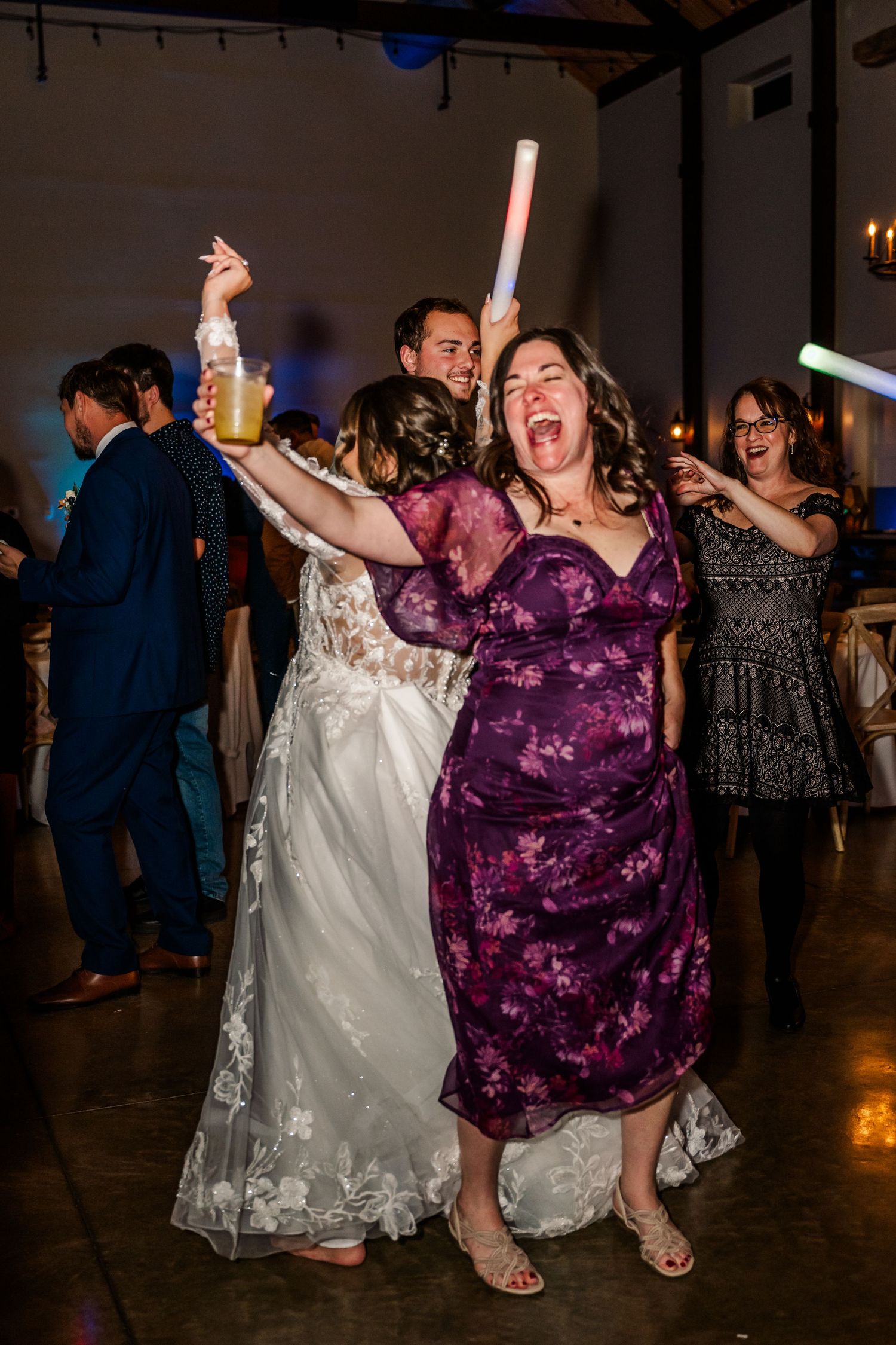 Wedding guests dancing and celebrating on the dance floor with glow sticks at an evening reception. Four Seasons Barn Wedding & Event Venue