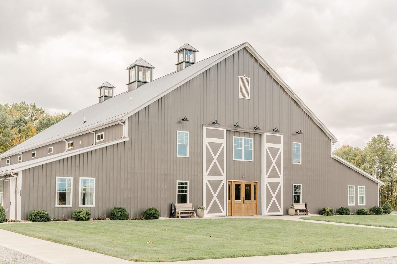 Modern gray barn-style wedding venue with white trim and multiple buildings set against a cloudy sky.Four Seasons Barn Wedding & Event Venue
