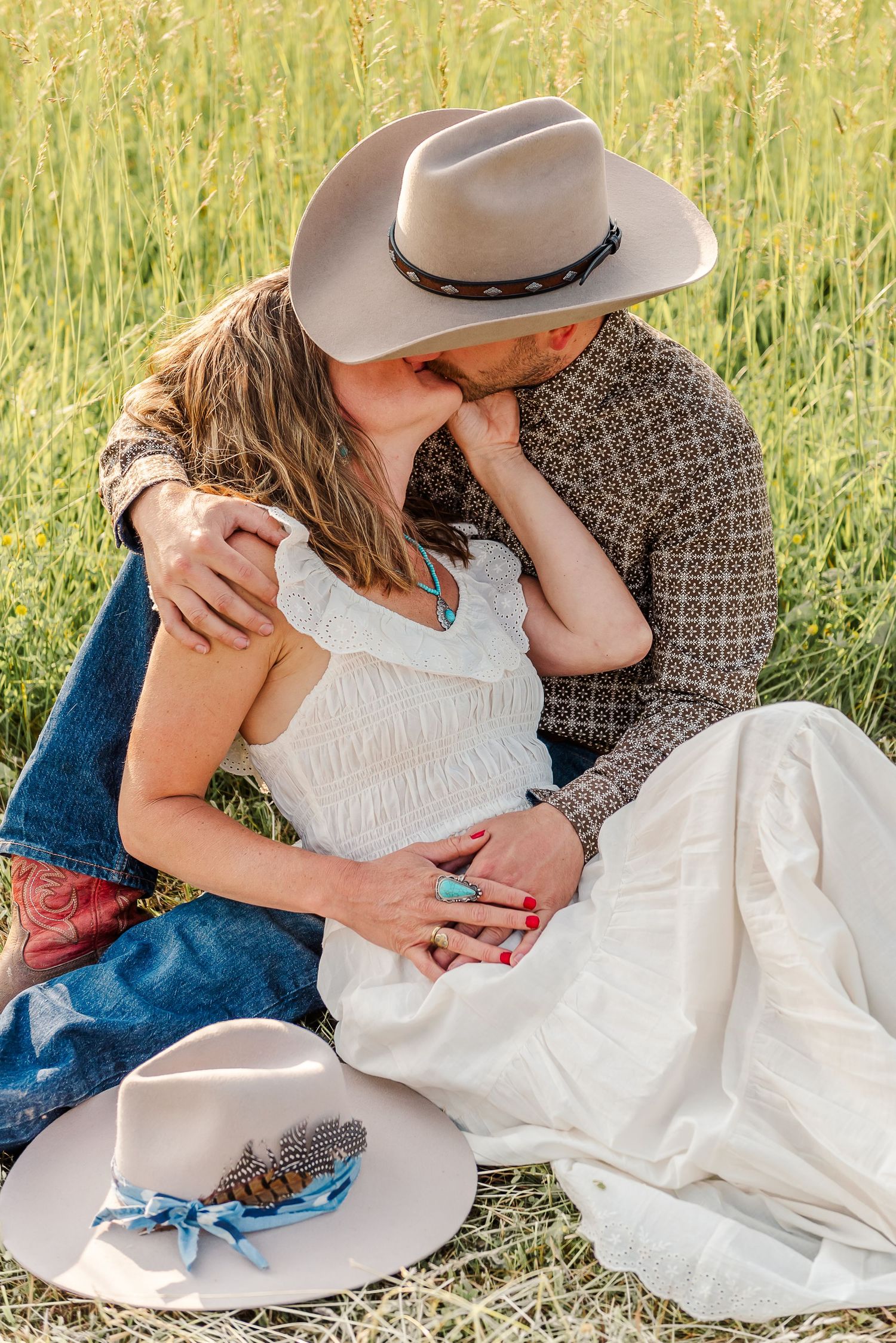 A romantic couple embraces in a golden wheat field wearing western attire and a white dress.