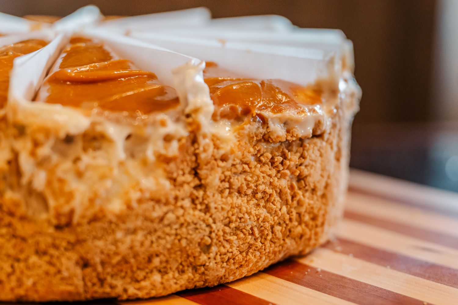 Close-up of a golden caramel cheesecake with white frosting drizzle on a wooden cutting board.