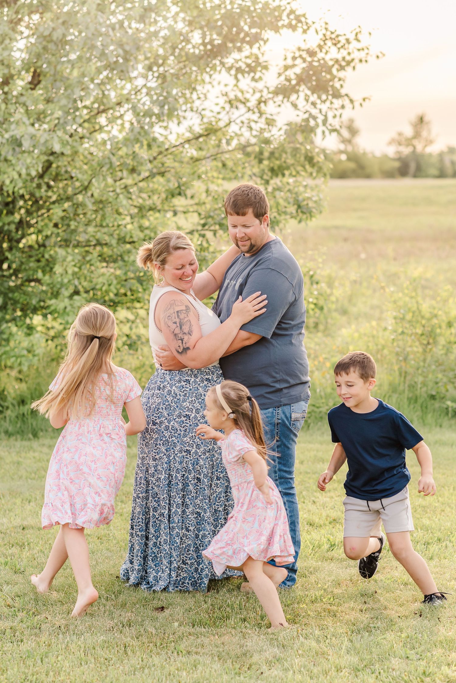 Family playing and dancing together in a sunlit field during golden hour photo session.