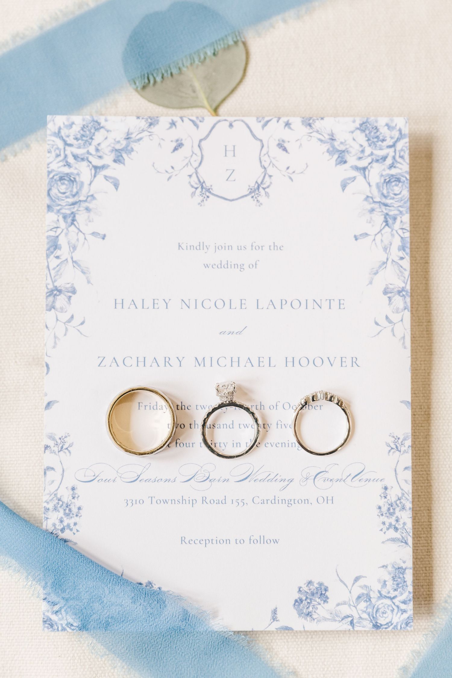 Elegant wedding invitation cards with delicate blue floral designs and wedding rings arranged on white surface