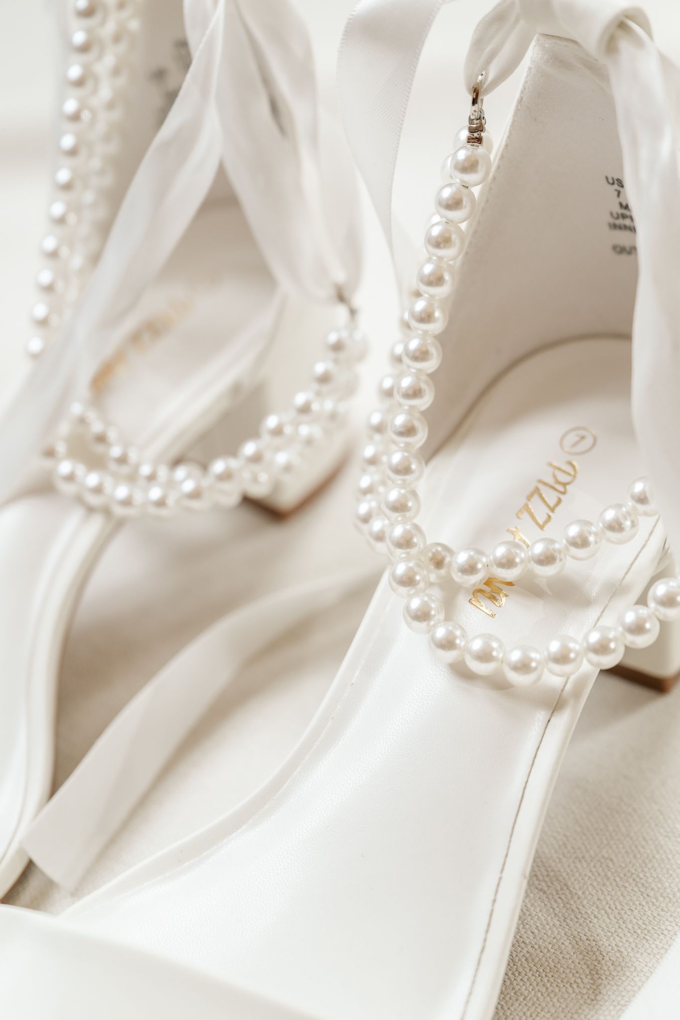 Elegant white bridal heels adorned with pearl straps and a delicate pearl necklace draped over them. The Crawford Barn wedding