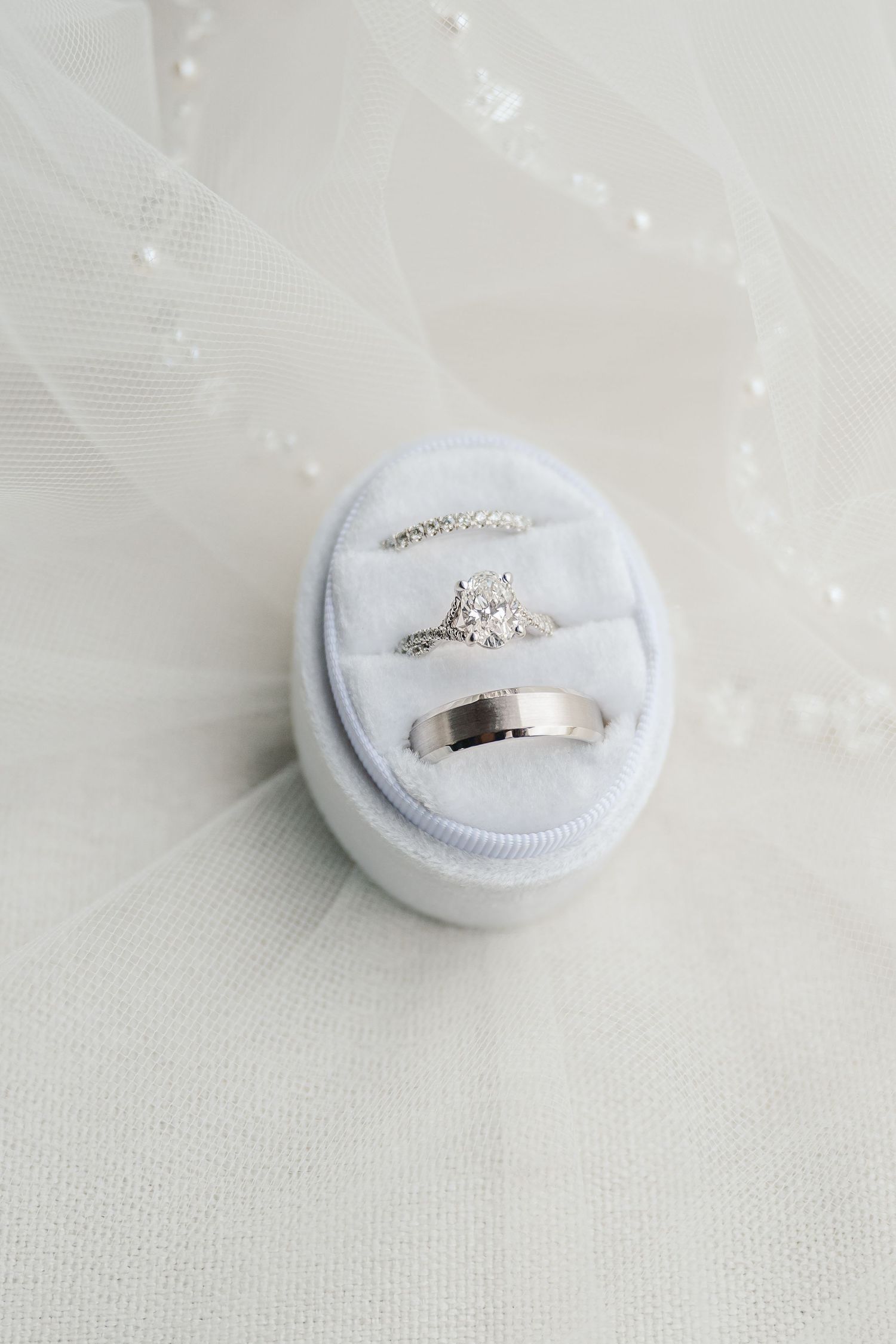 Wedding rings displayed in a white velvet ring box on a light fabric background.