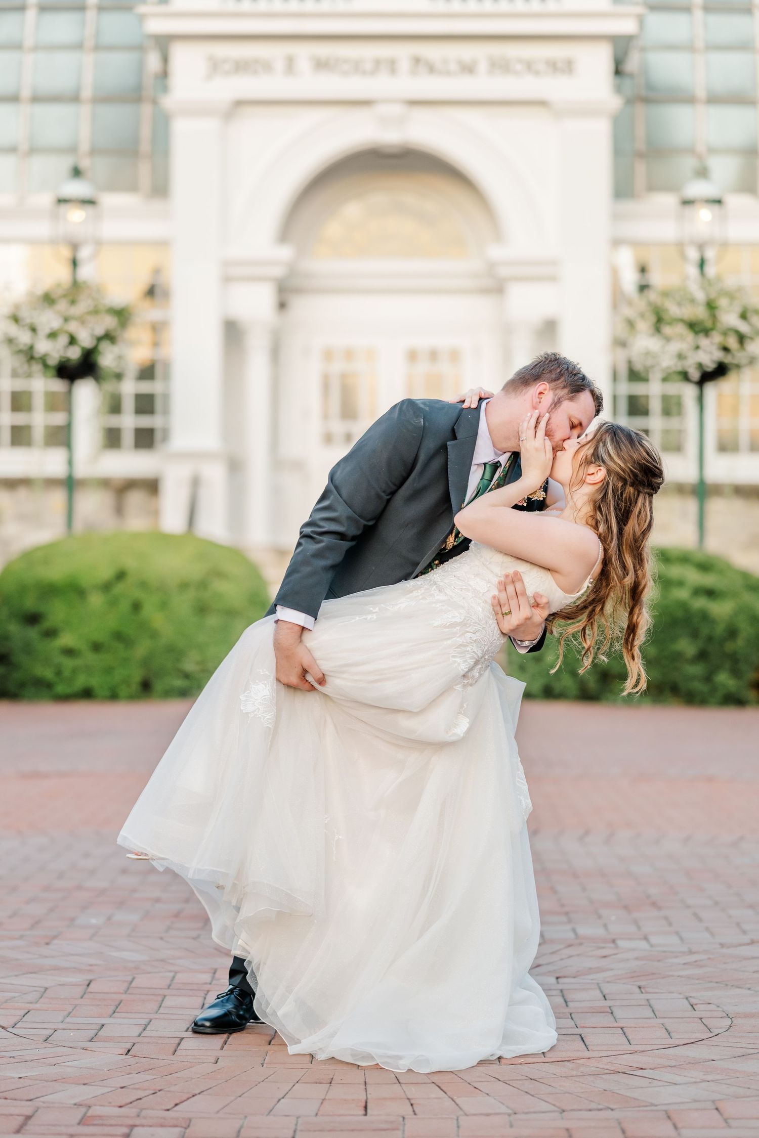 A romantic wedding photo showing a dip kiss pose in front of an elegant archway.