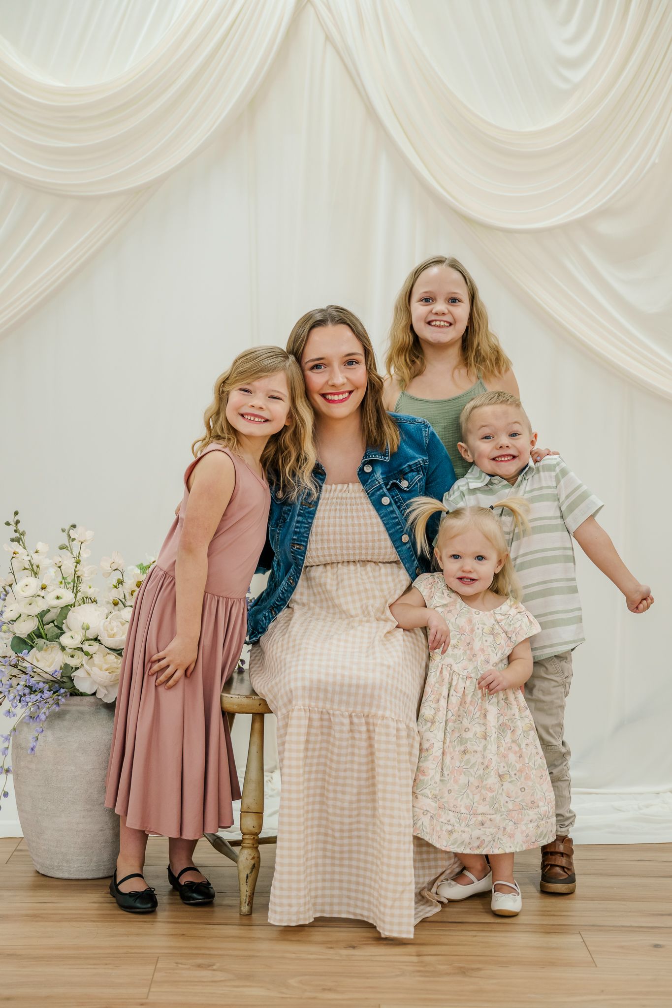 A group poses together in front of white draped fabric with floral arrangements and coordinated spring outfits.