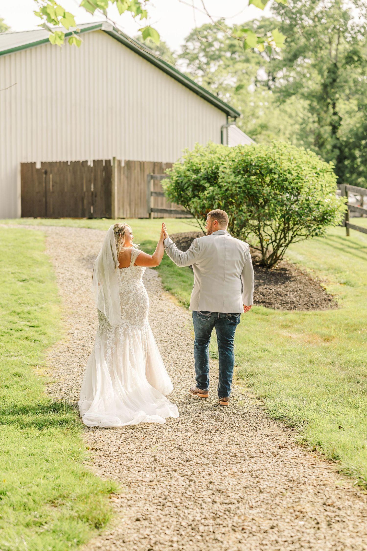 Couple walking down a gravel path after their wedding ceremony with rustic buildings in the background.