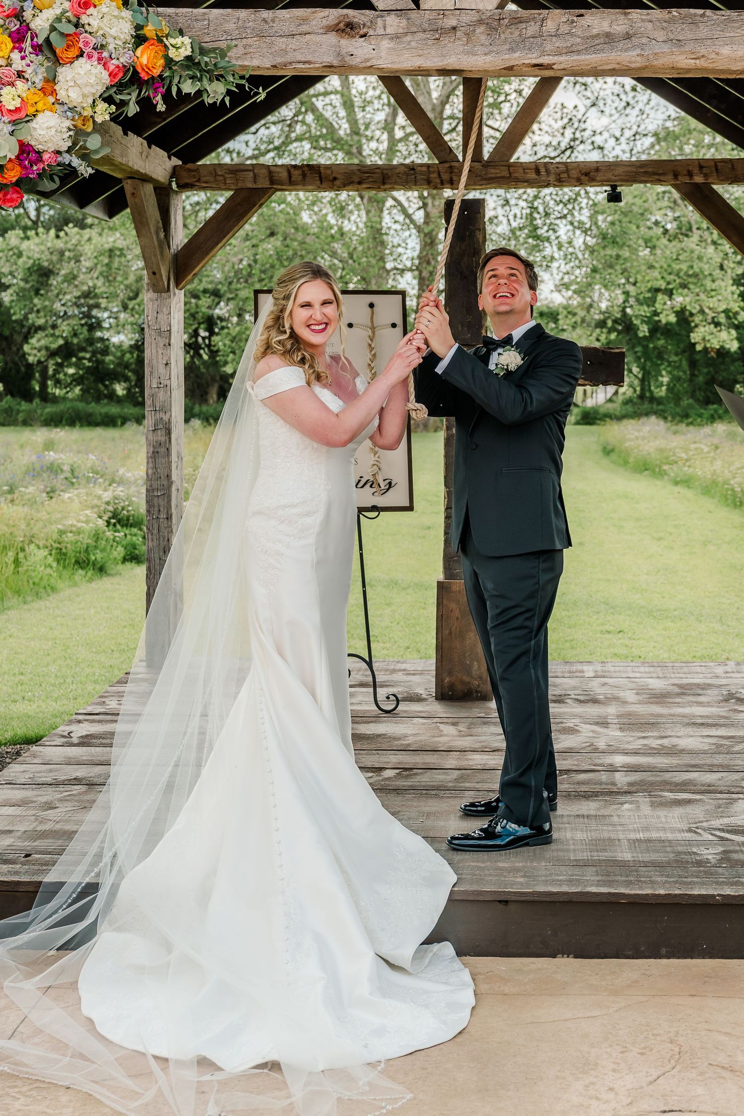 A couple shares their first dance under a rustic wooden pavilion decorated with colorful floral arrangements.