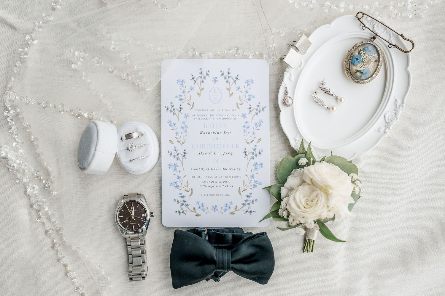 Elegant wedding details flatlay with invitation, rings, bow tie, flowers and delicate accessories on light gray background.