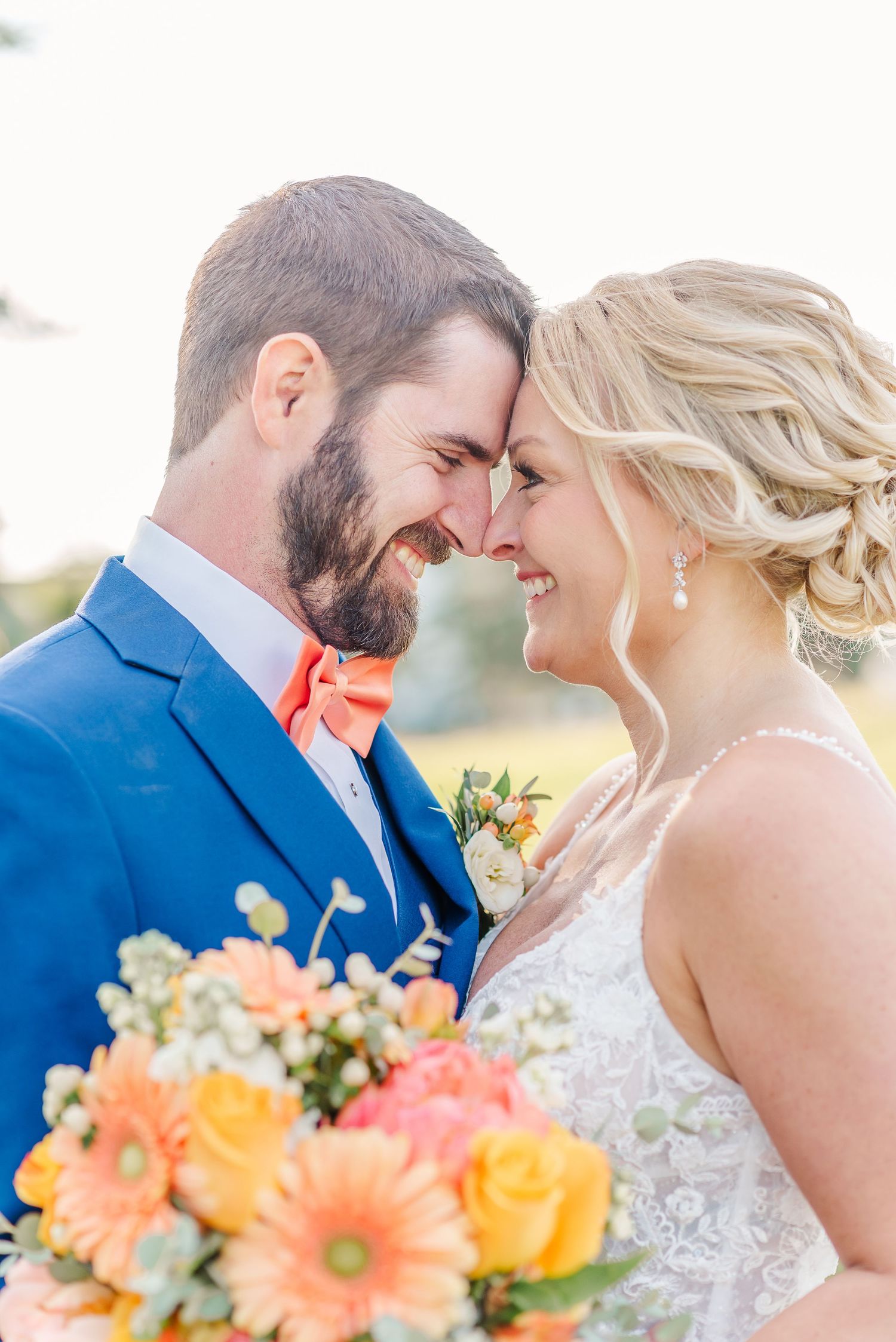 Sunlit wedding portrait with vibrant coral and yellow flowers in foreground.
