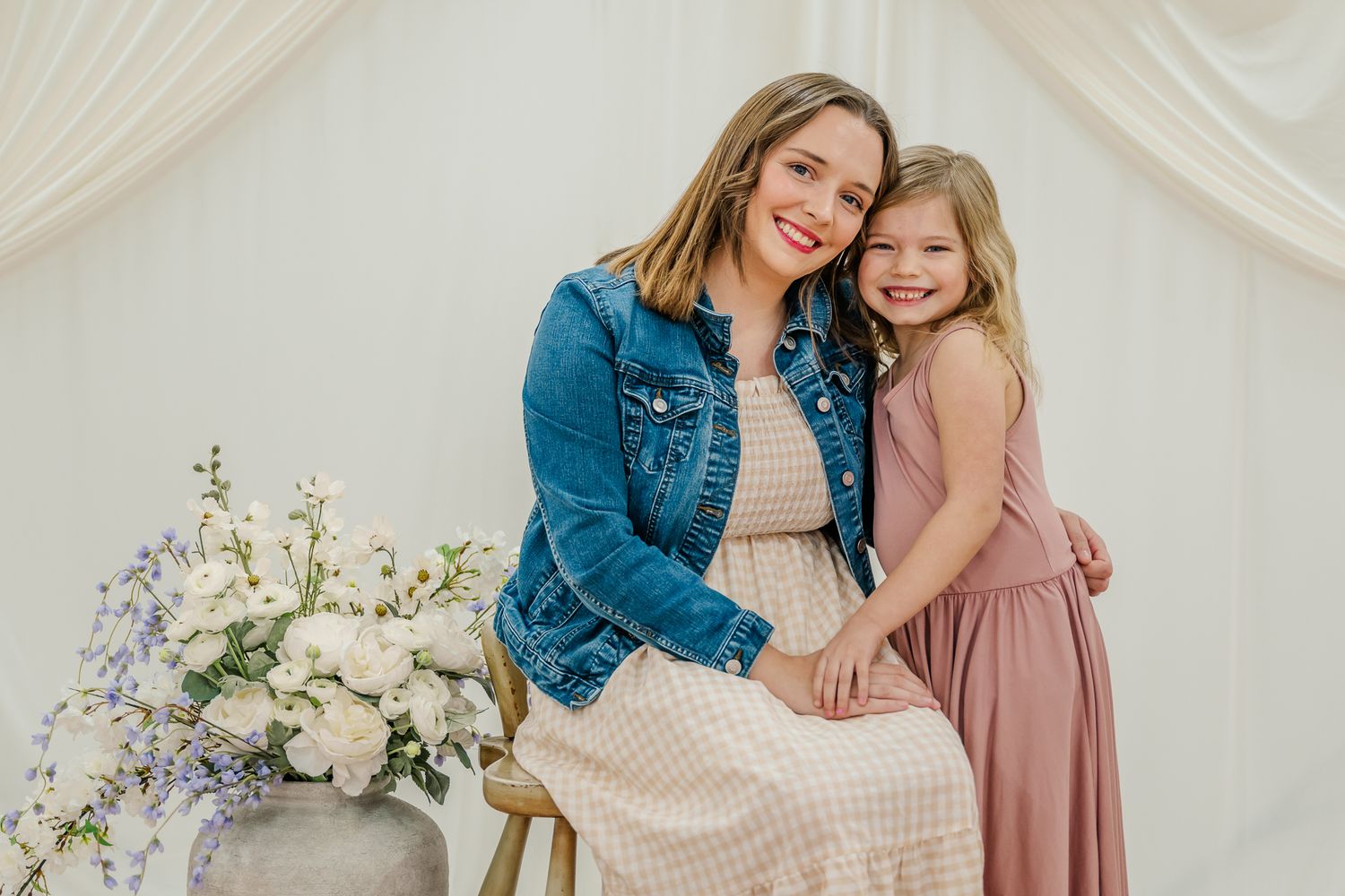 A mother and daughter share affectionate moments in coordinated outfits during a light and airy indoor photo session.