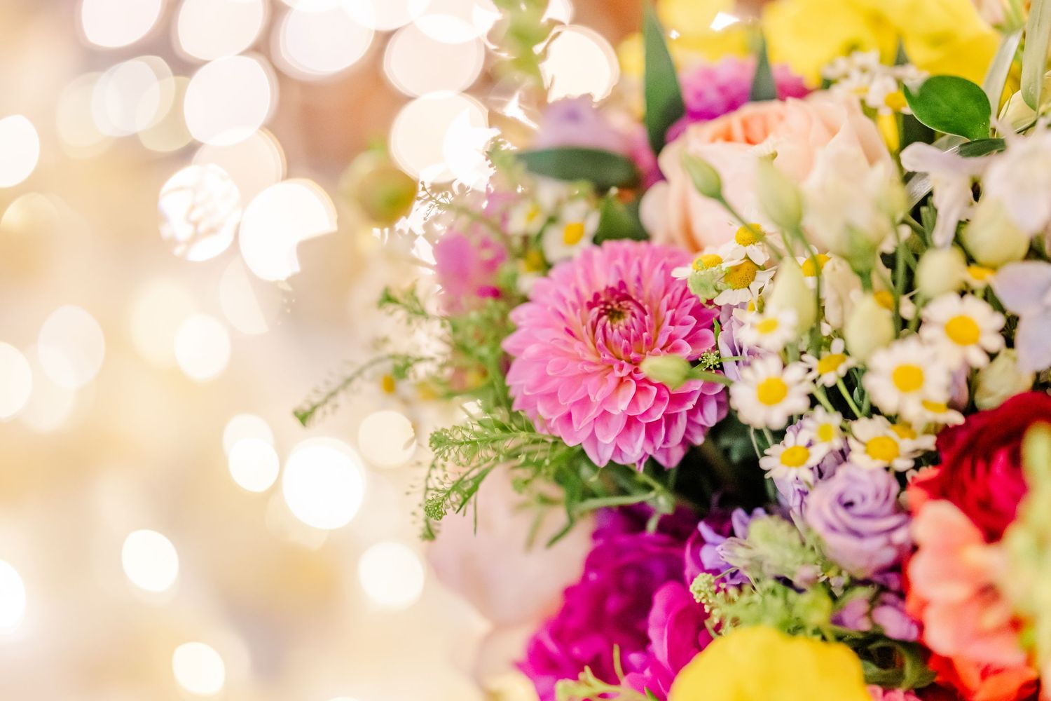 Colorful assortment of fresh flowers including pink, yellow, and purple blooms with soft bokeh background effect.