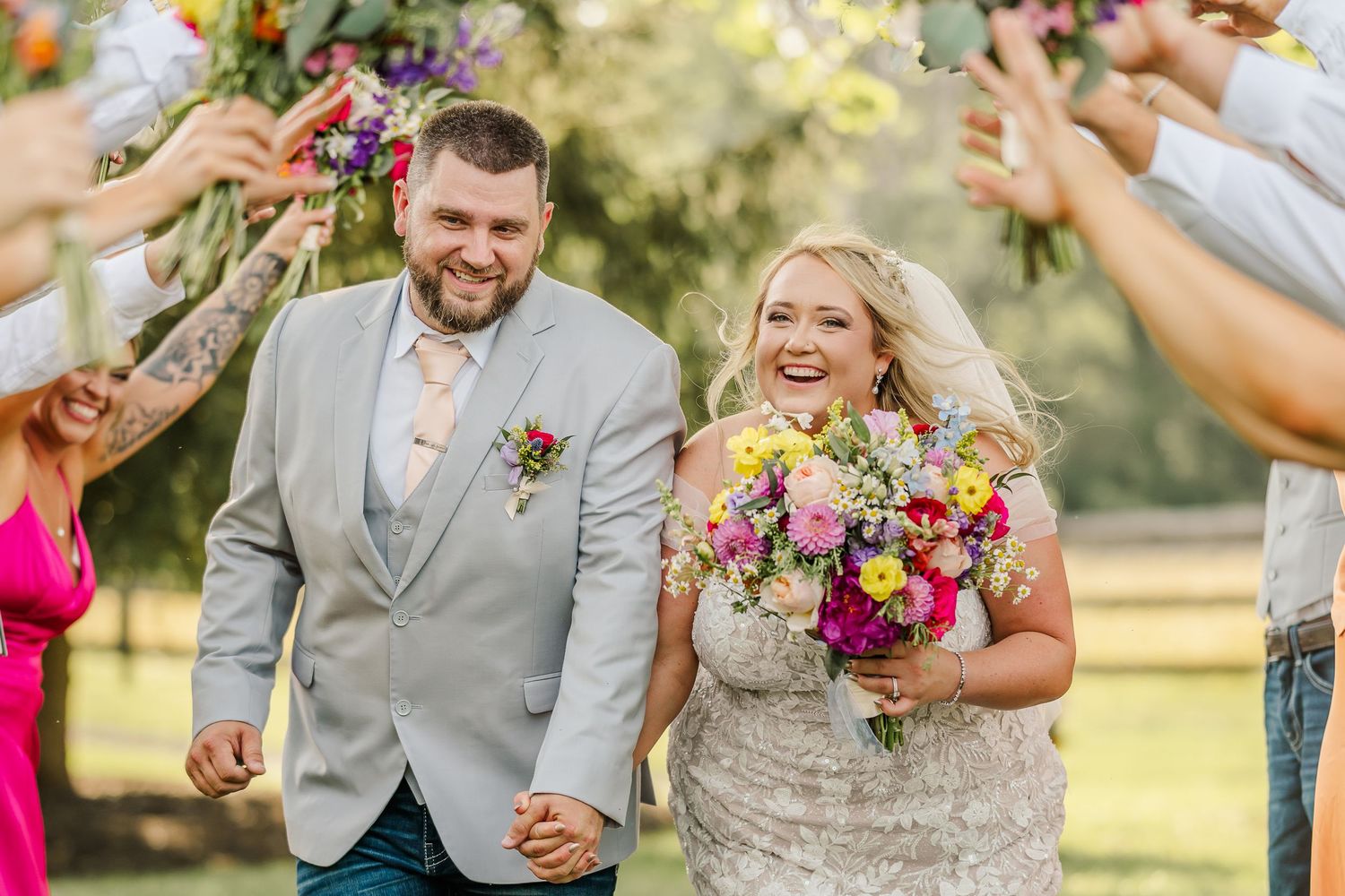 Newlyweds walk down aisle while guests throw flower petals in joyful outdoor wedding celebration.