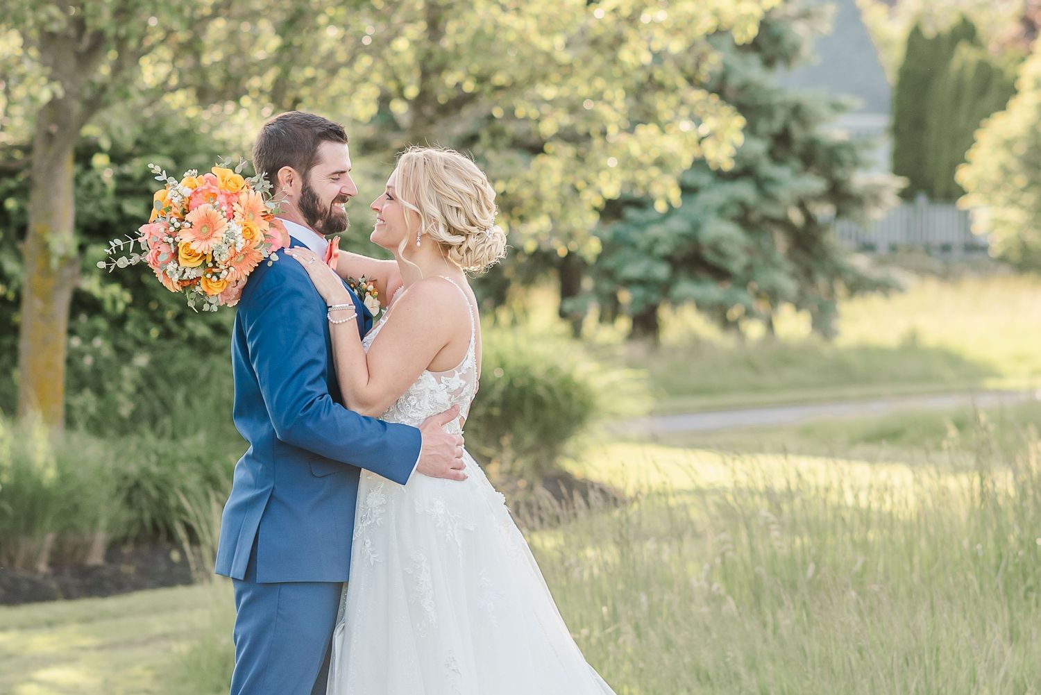 A couple shares a romantic moment during their outdoor wedding photoshoot in a sunlit garden setting.