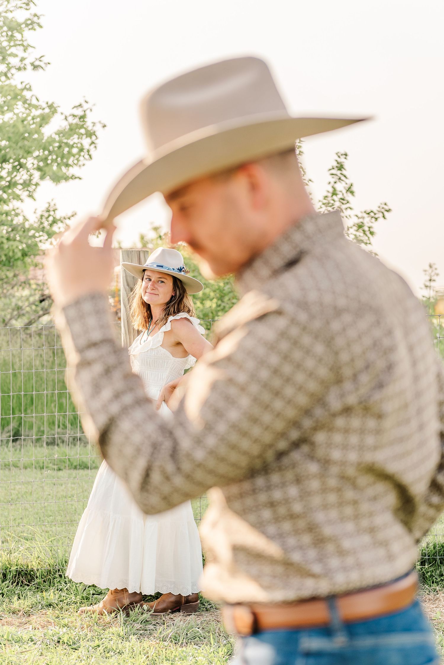 A romantic couple shares an intimate moment in a sunlit field wearing western-style clothing.