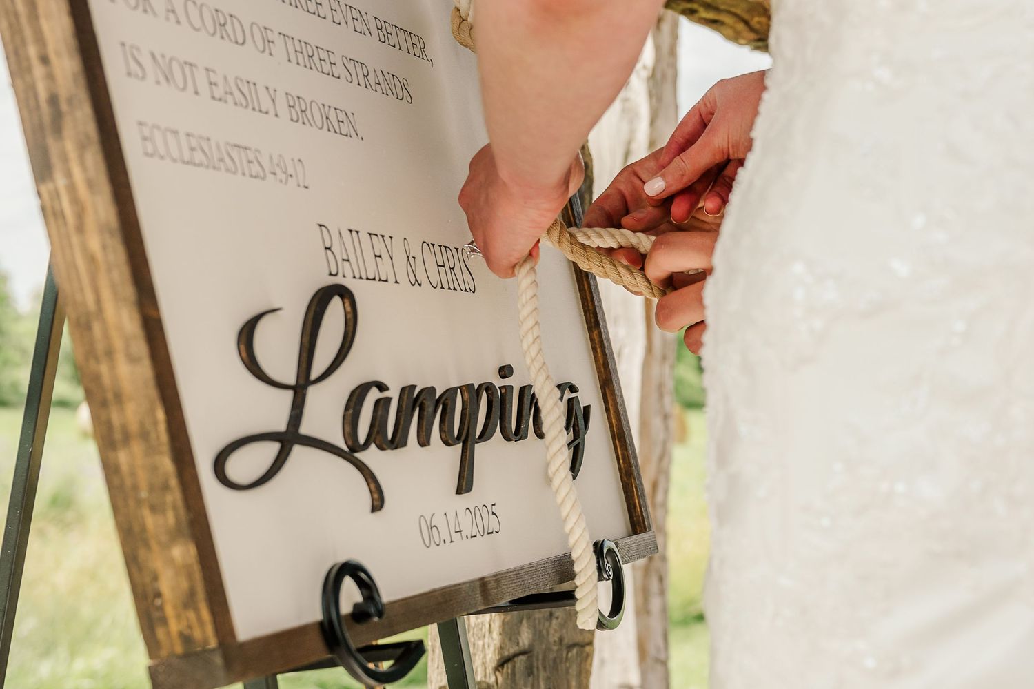 A couple signs their names in a wedding guest book with a decorative pen at an outdoor ceremony.