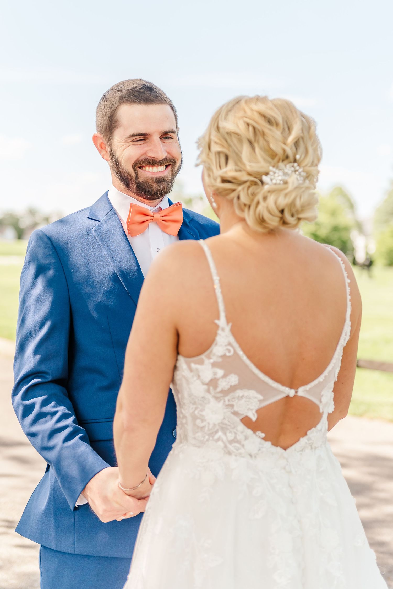 A couple shares a joyful moment during their outdoor wedding ceremony, with the groom in a blue suit and coral bowtie.