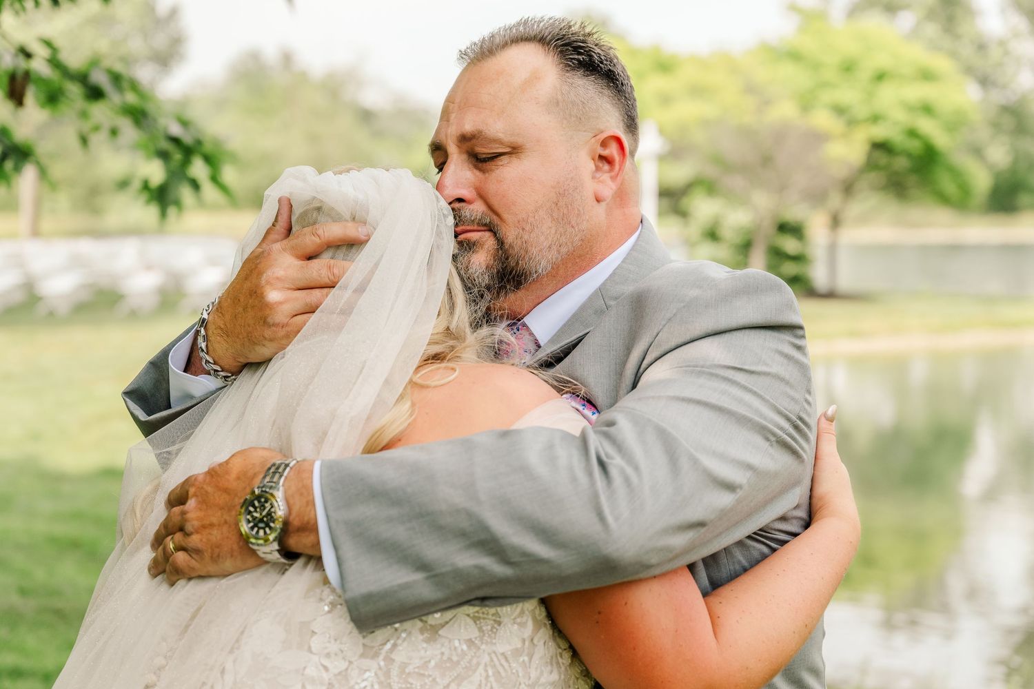 A romantic moment between a couple in formal attire embracing by a scenic lake on their wedding day.