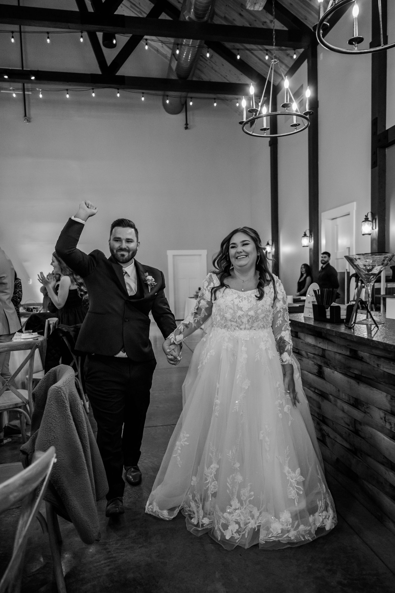 A joyful newlywed couple makes their grand entrance into their wedding reception venue with raised hands.